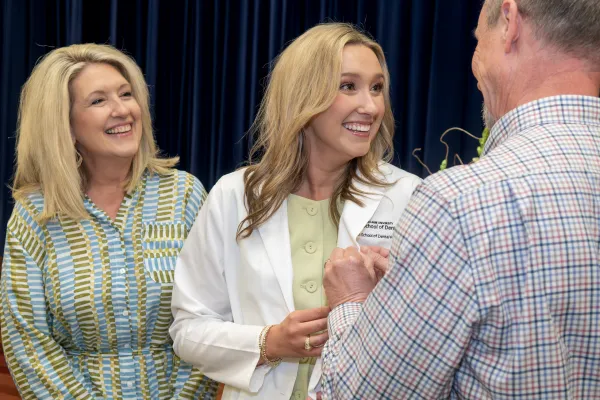 A dental hygiene student in a white coat celebrates with family members at a pinning or white coat ceremony