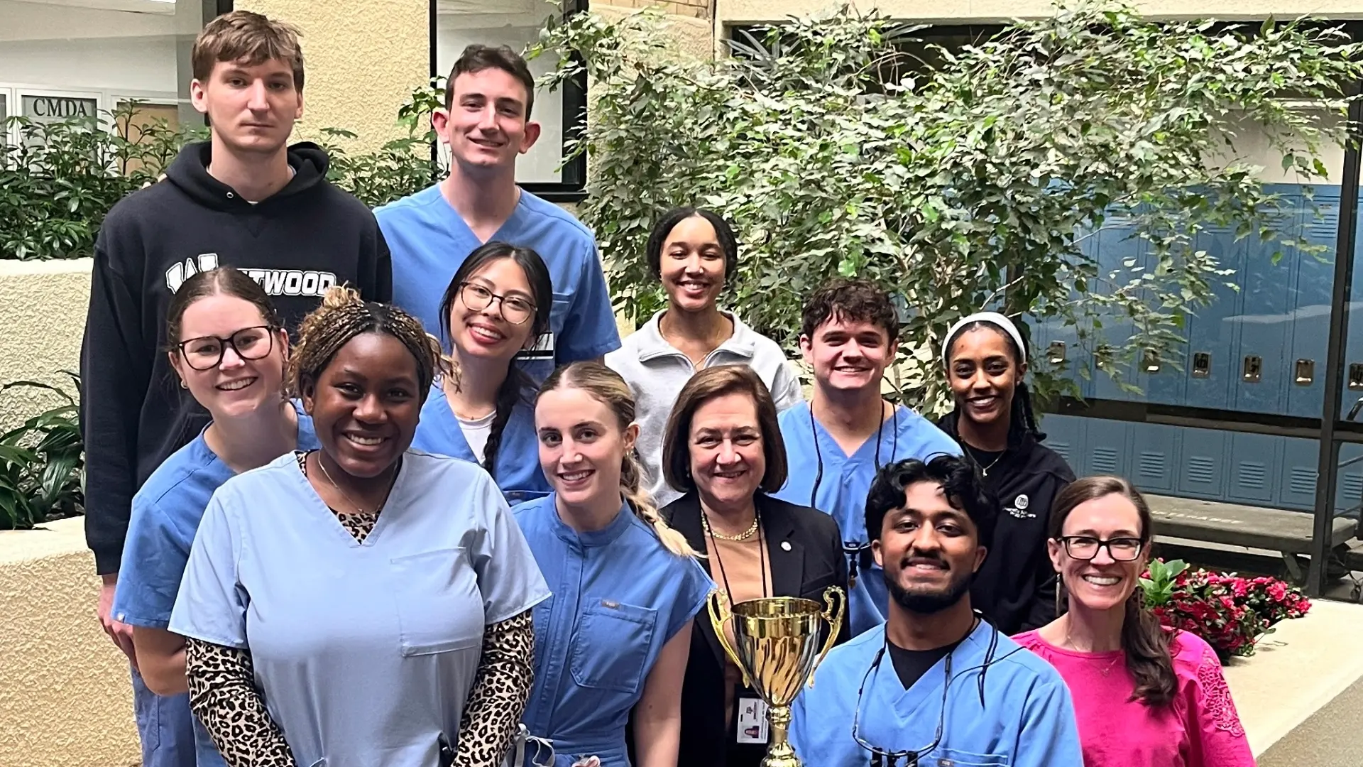 Group photo of dental students and faculty standing in the atrium of Texas A&M Dentistry with a trophy.