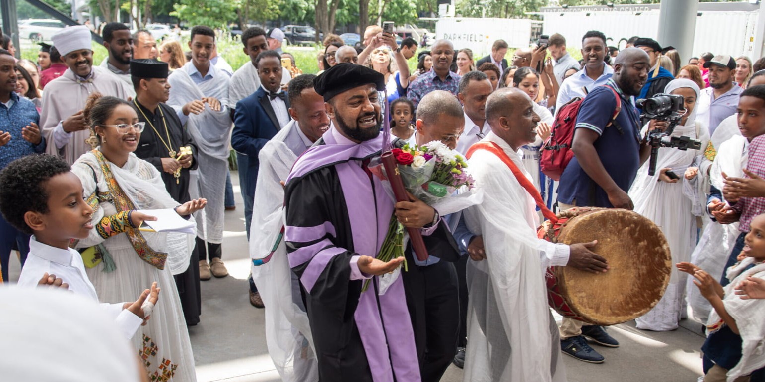 A dental school graduate in cap and gown is joyfully celebrated by family and community members after commencement.