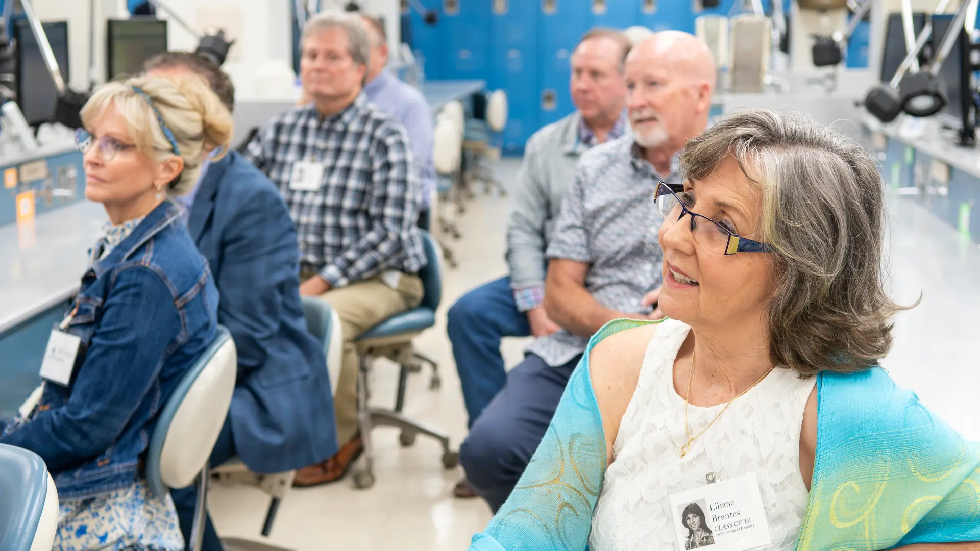 Group of dental school alumni seated in a laboratory during a class reunion.