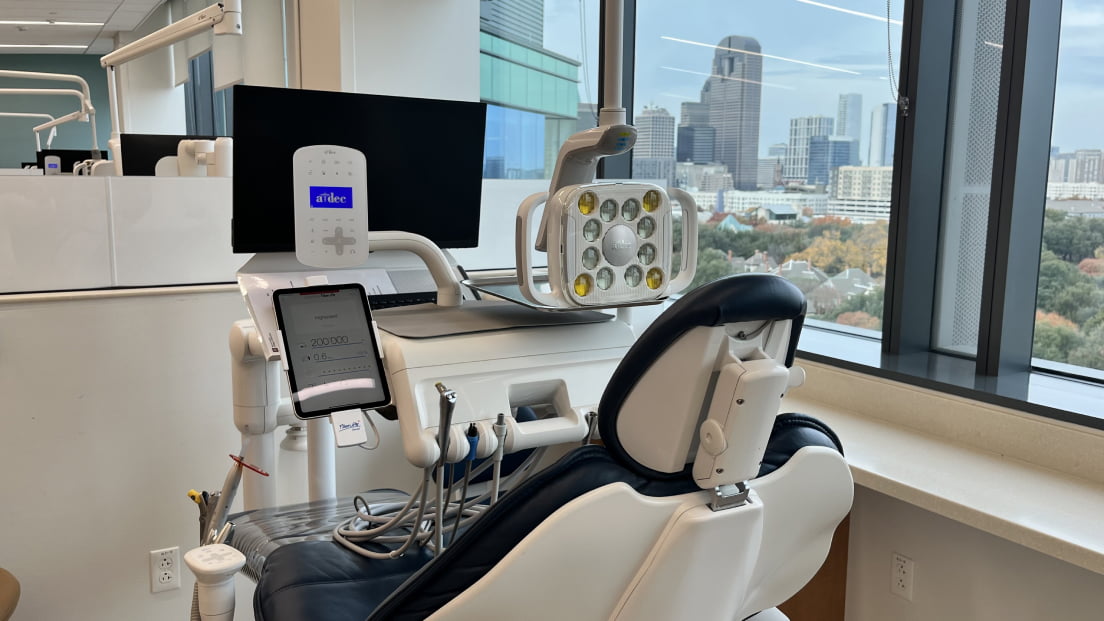 A modern dental treatment chair and equipment station with a city skyline visible through floor-to-ceiling windows.