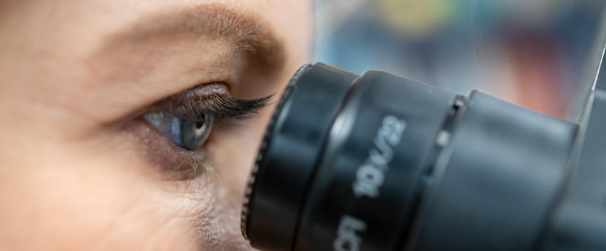 A close-up of a researcher looking through a microscope eyepiece.