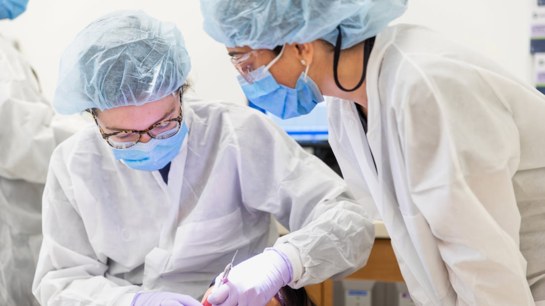 Two dental students in full protective gear work together on a clinical procedure.