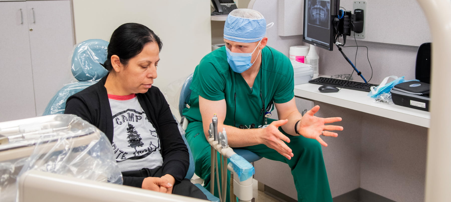 A dental provider consults with a patient seated in a dental chair.