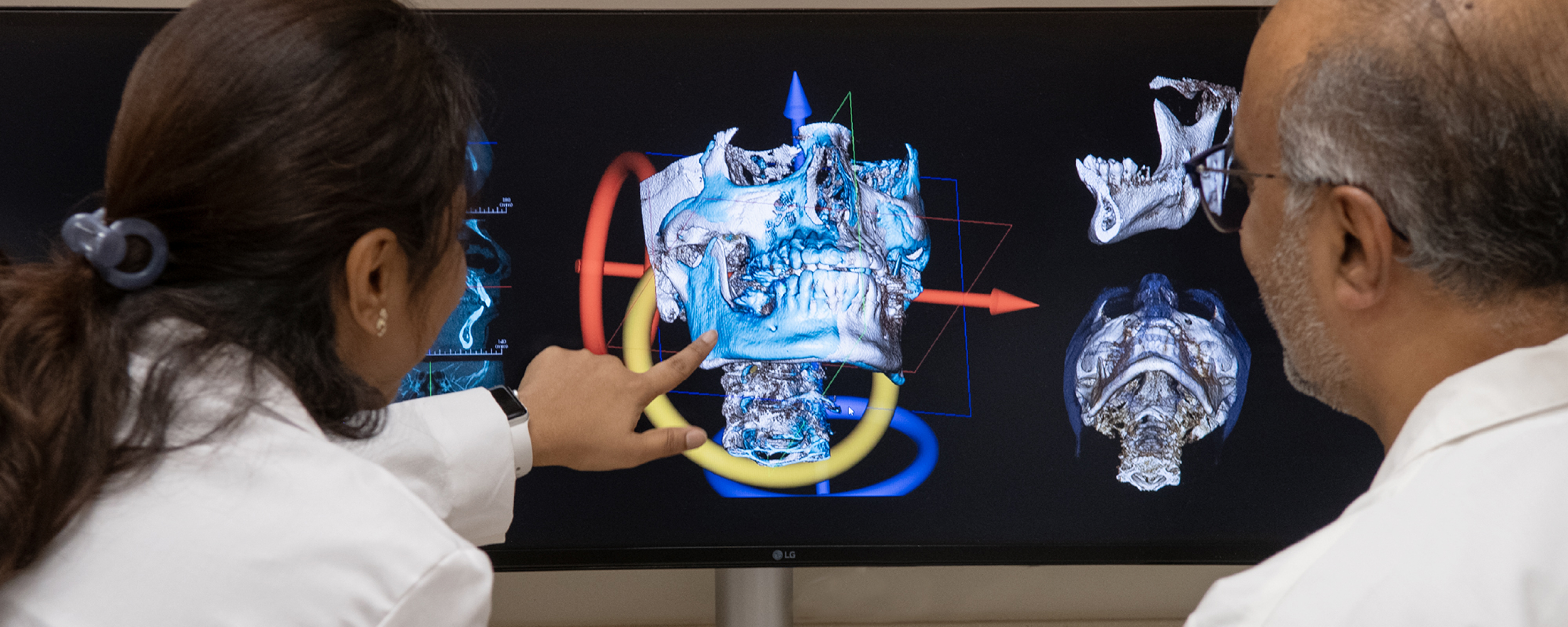 Dental professionals analyzing a 3D digital skull reconstruction and diagnostic imaging on a large monitor.
