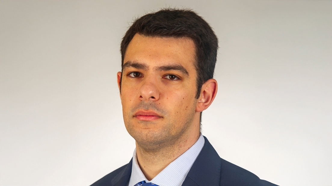 Profile headshot of Ioakeim Flevotomas wearing a blue suit and tie against a gray background.