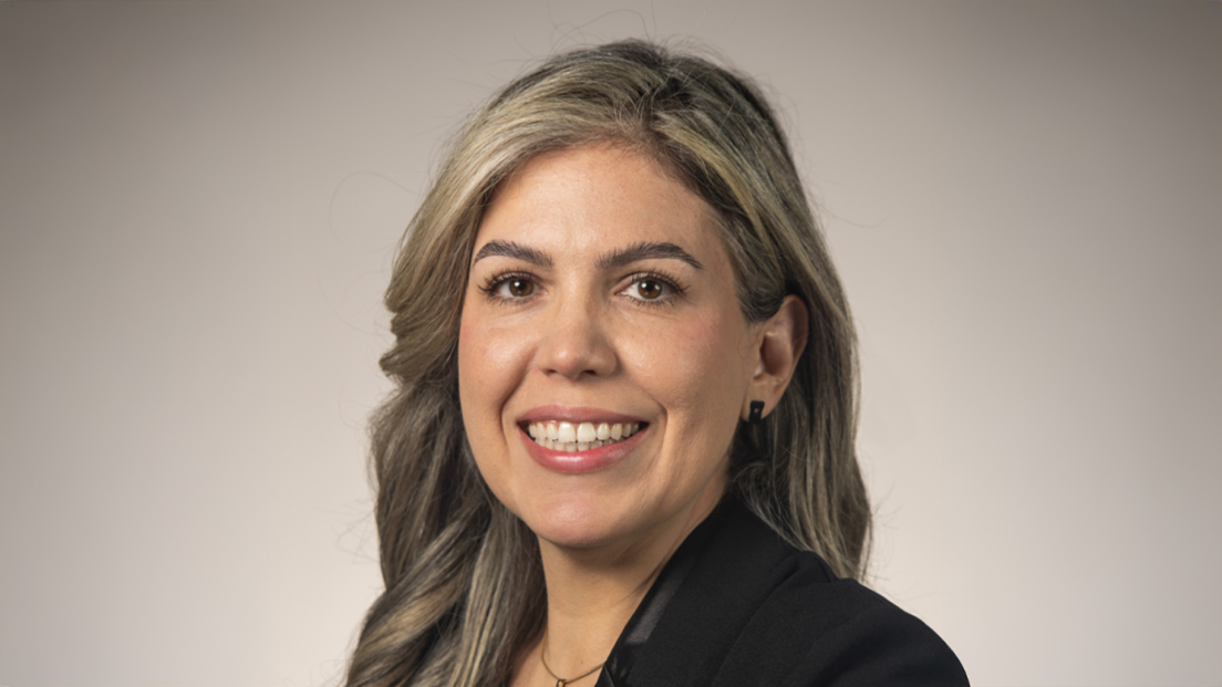 Profile headshot of Karina Caia Lemos smiling against a gray background.