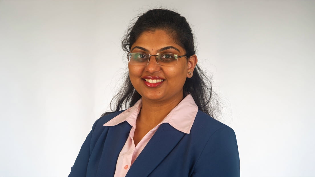 Profile headshot of Madhulika Sarvepalli wearing a blue blazer and glasses, smiling against a gray background.