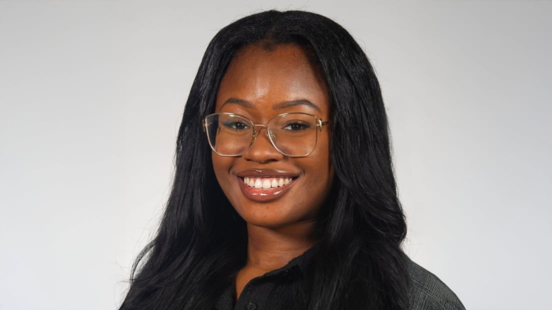 Profile headshot of Monique Duru wearing glasses and smiling against a gray background.