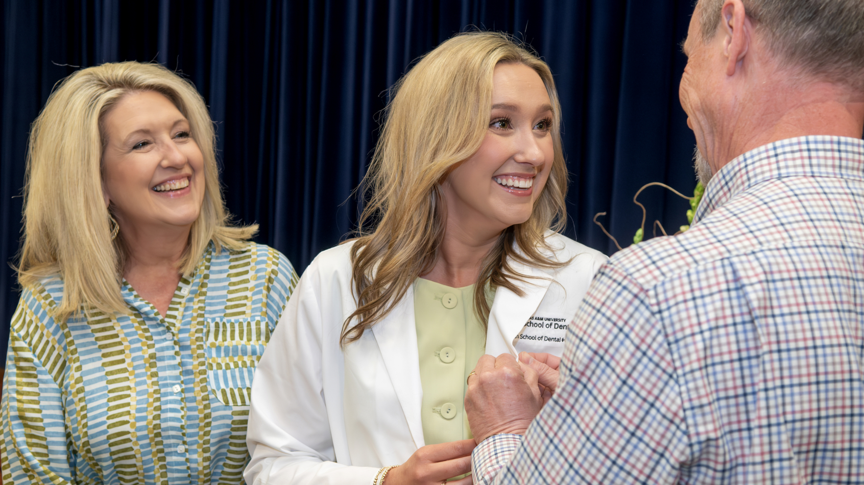 A dental hygiene or education graduate smiling warmly alongside family members during an institutional ceremony.