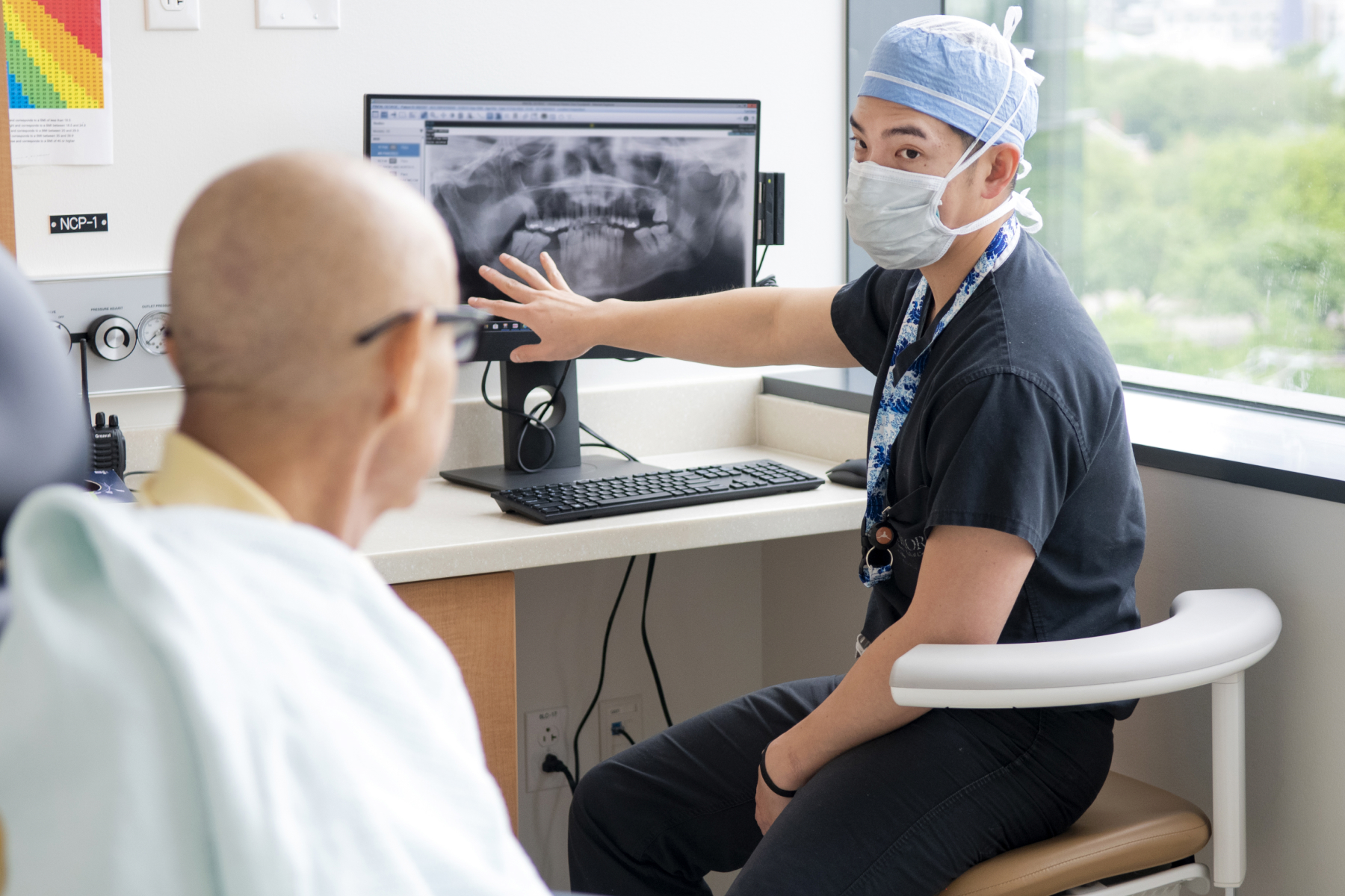 A surgical resident or practitioner explaining a panoramic X-ray to a patient in a dental clinic.