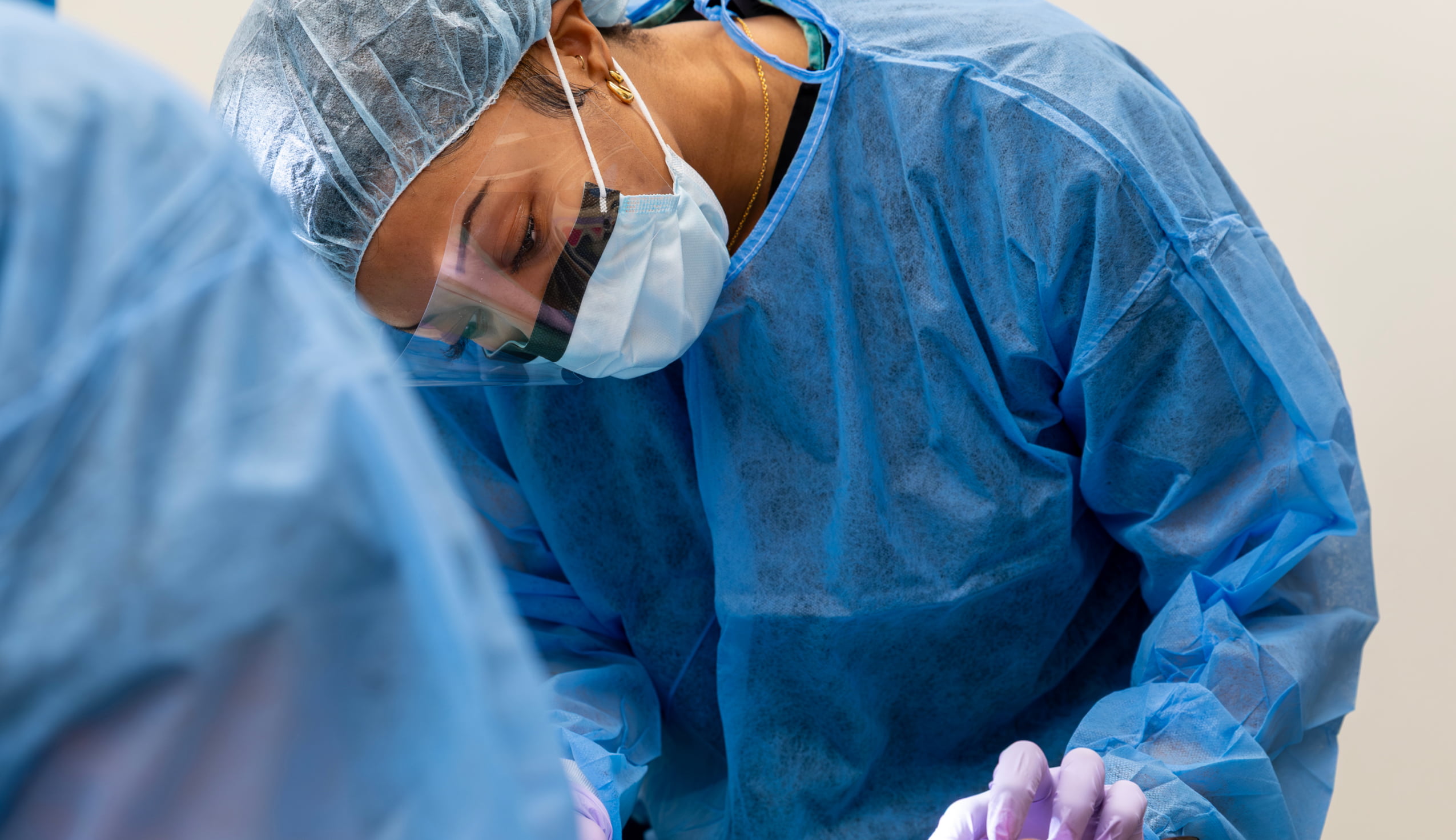 An oral surgery resident or practitioner wearing protective gear, a mask, and a face shield during a surgical procedure.