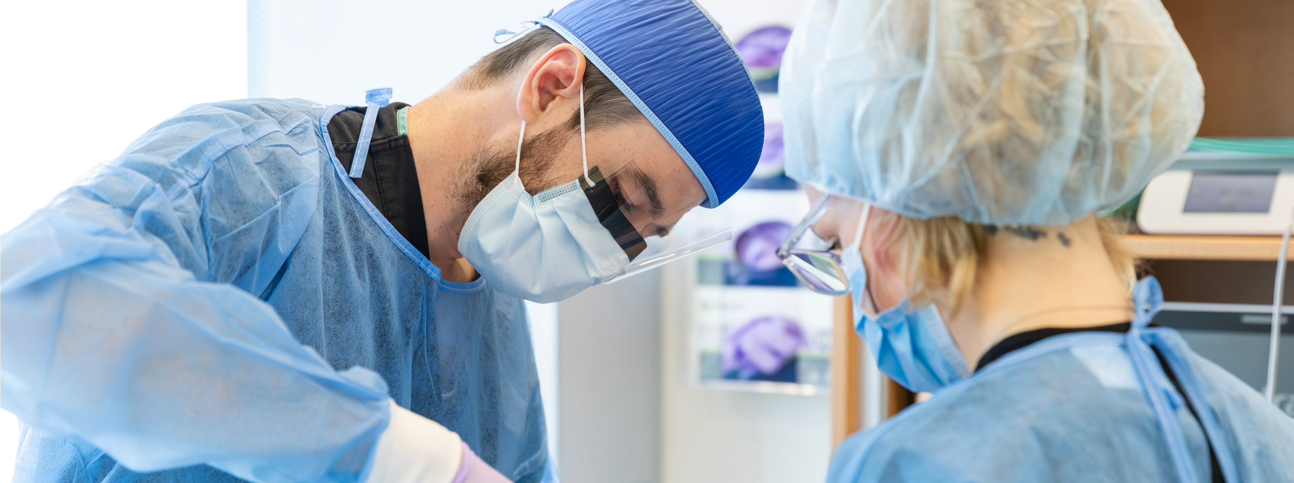 Two oral surgery practitioners in full sterile surgical gear focused intently on a patient procedure.
