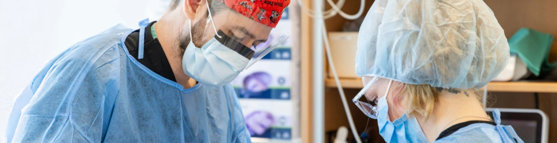 Two oral surgery providers in full surgical attire perform a procedure together.
