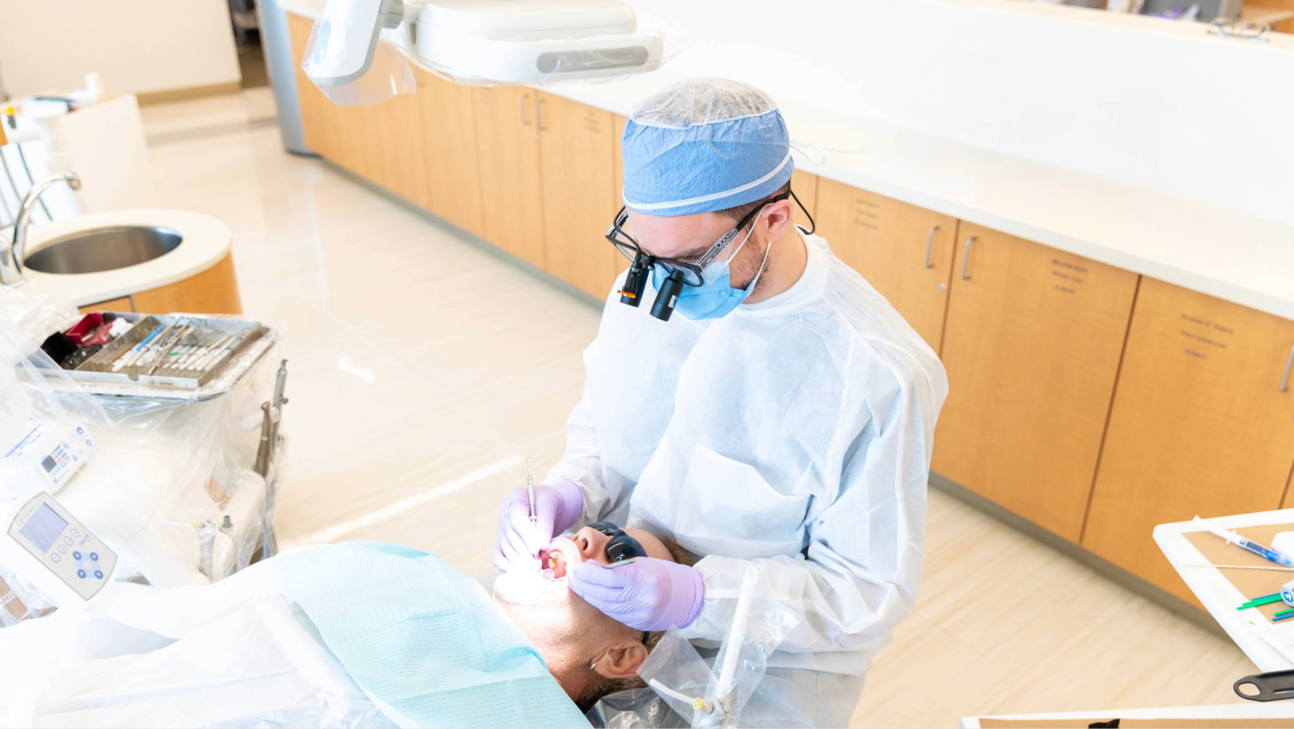 A dental resident wearing protective gear and magnification loupes performing a procedure on a patient in a modern clinic.