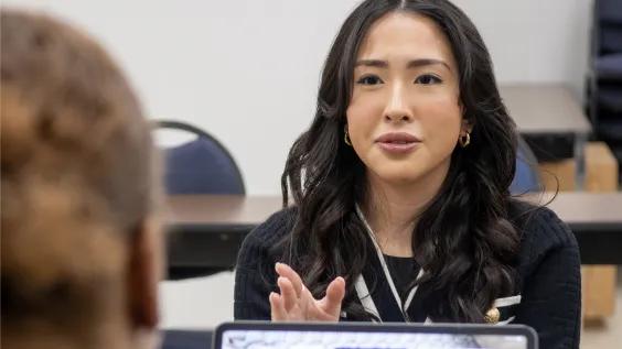 A young woman with a name badge speaks and gestures during a meeting or classroom discussion.