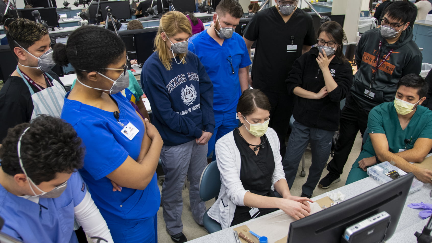 A dental practitioner in blue scrubs gesturing and speaking with a colleague in a white lab coat during a professional presentation event.