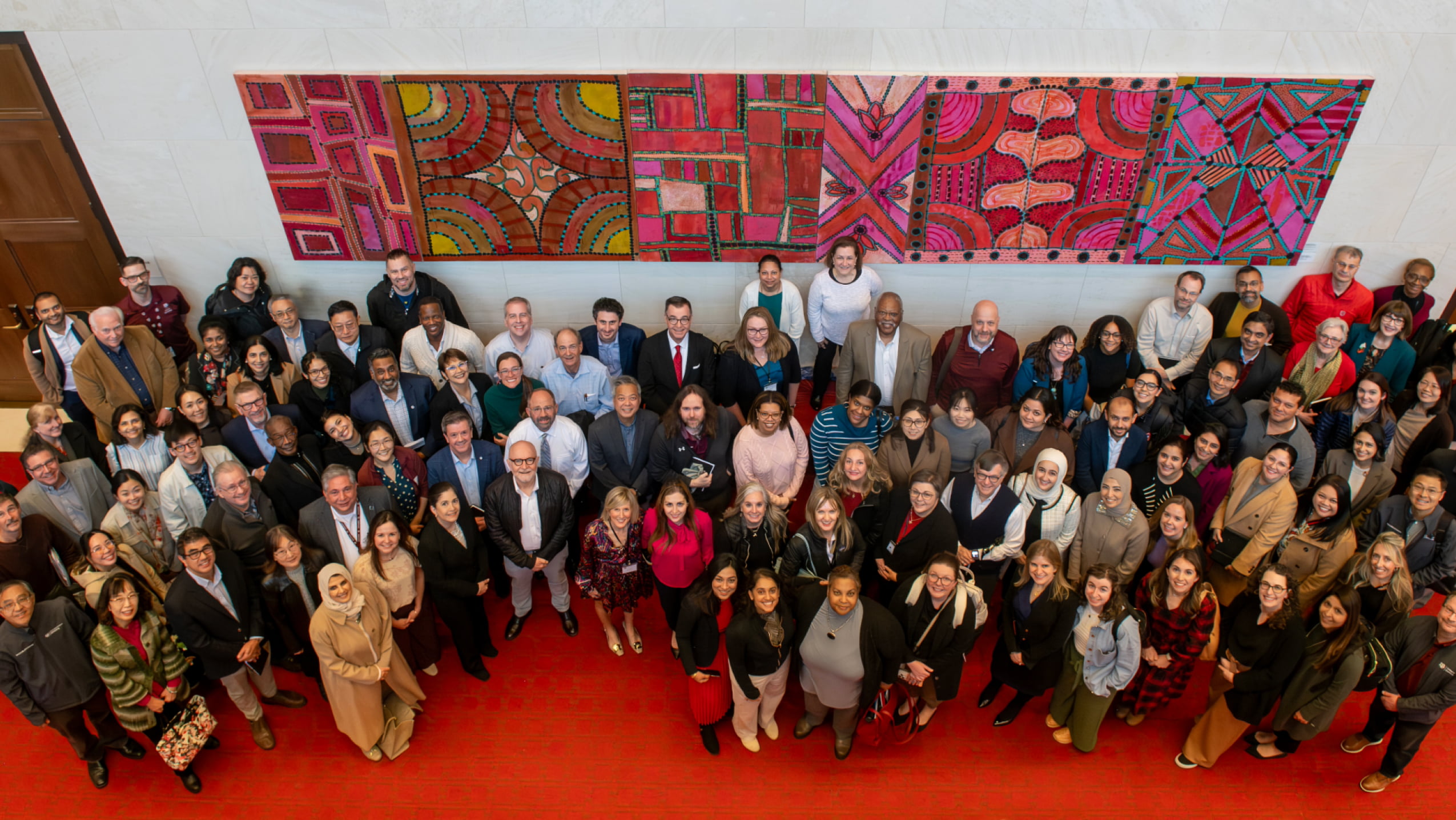 A large group of diverse dental school faculty and staff posing together for a group portrait in front of a vibrant, colorful abstract mural.