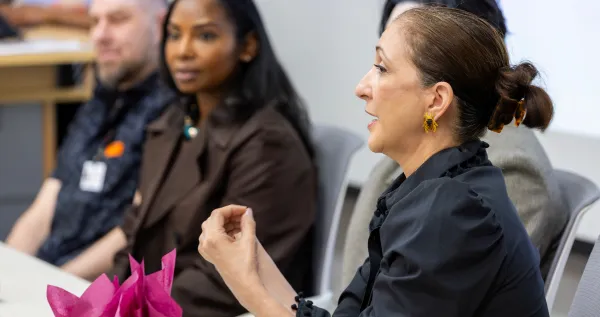 A woman speaks during a panel or group discussion, with two other attendees seated behind her.