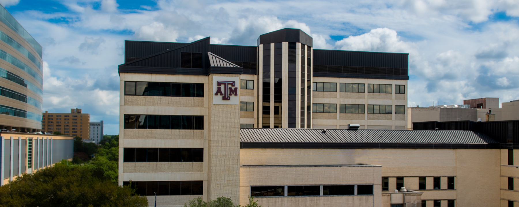 A wide panoramic shot of the exterior of the Texas A&M University College of Dentistry building on a partly cloudy day.