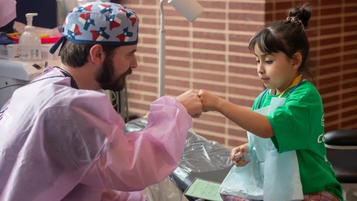 A dental student fist-bumps a young child during a community dental outreach event.