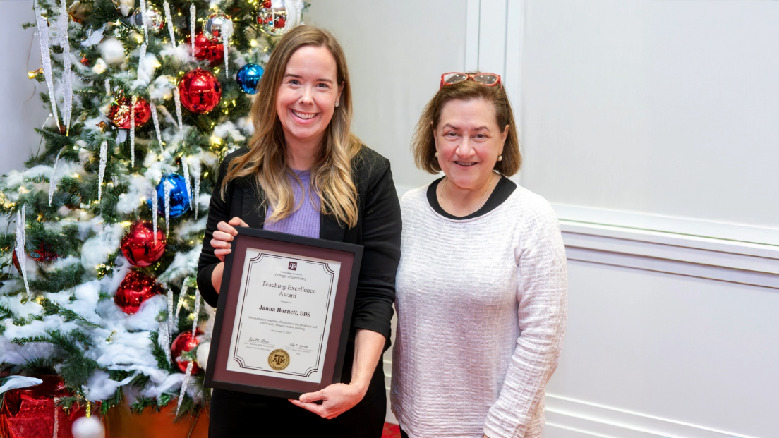 Janna Burnett, DDS, smiling alongside a colleague while proudly holding her framed Teaching Excellence Award in front of a decorated holiday tree.